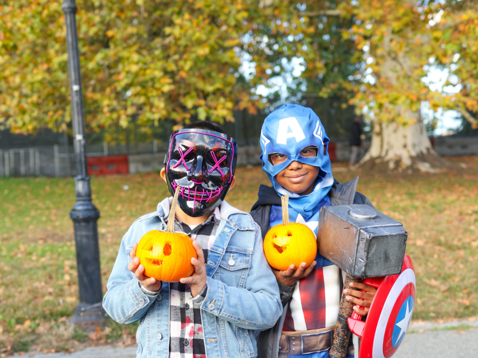 Two kids in Halloween dress hold up pumpkins in Central Park